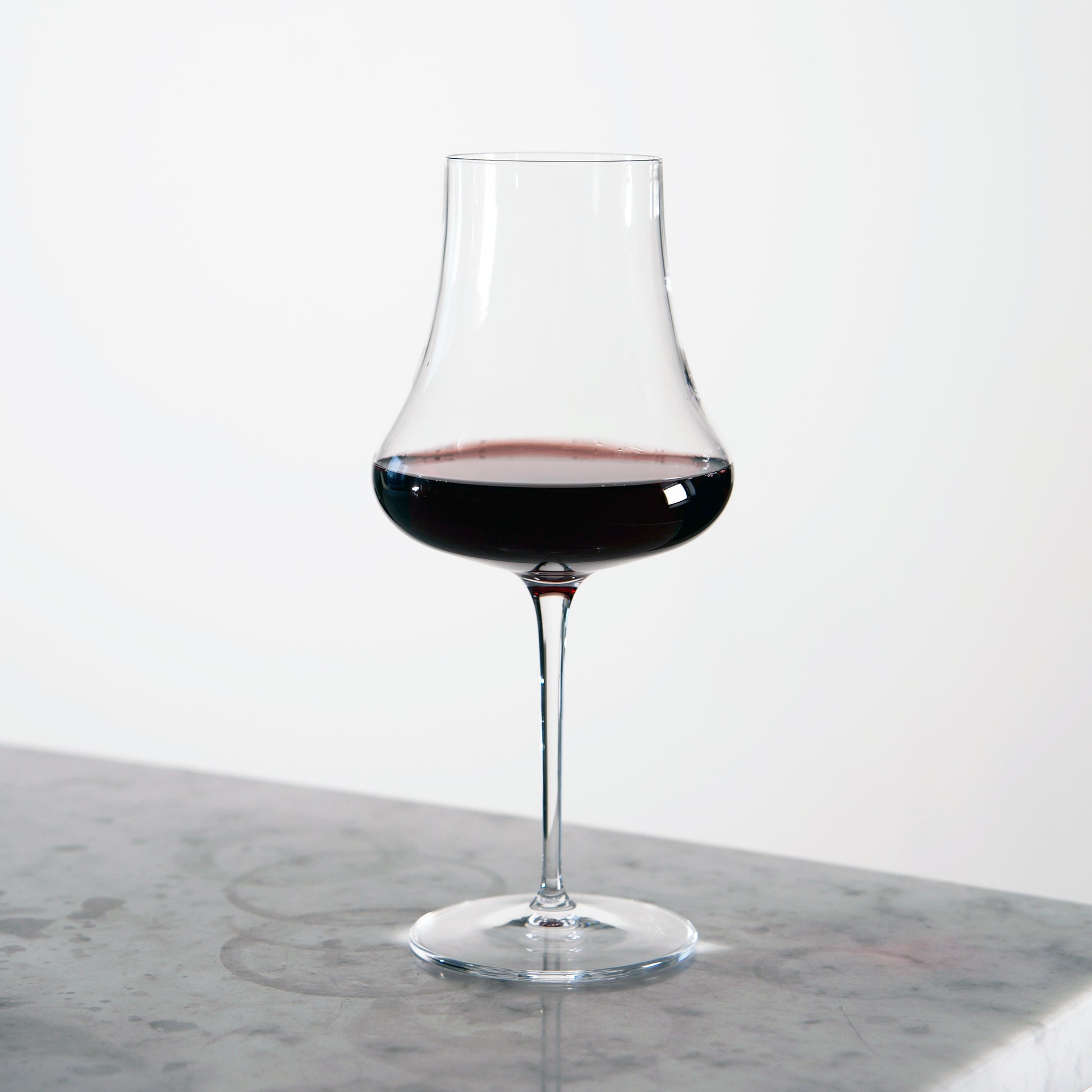 Tentazioni Bordeaux Red Wine Glass filled with red wine standing on a light marble surface and a white background