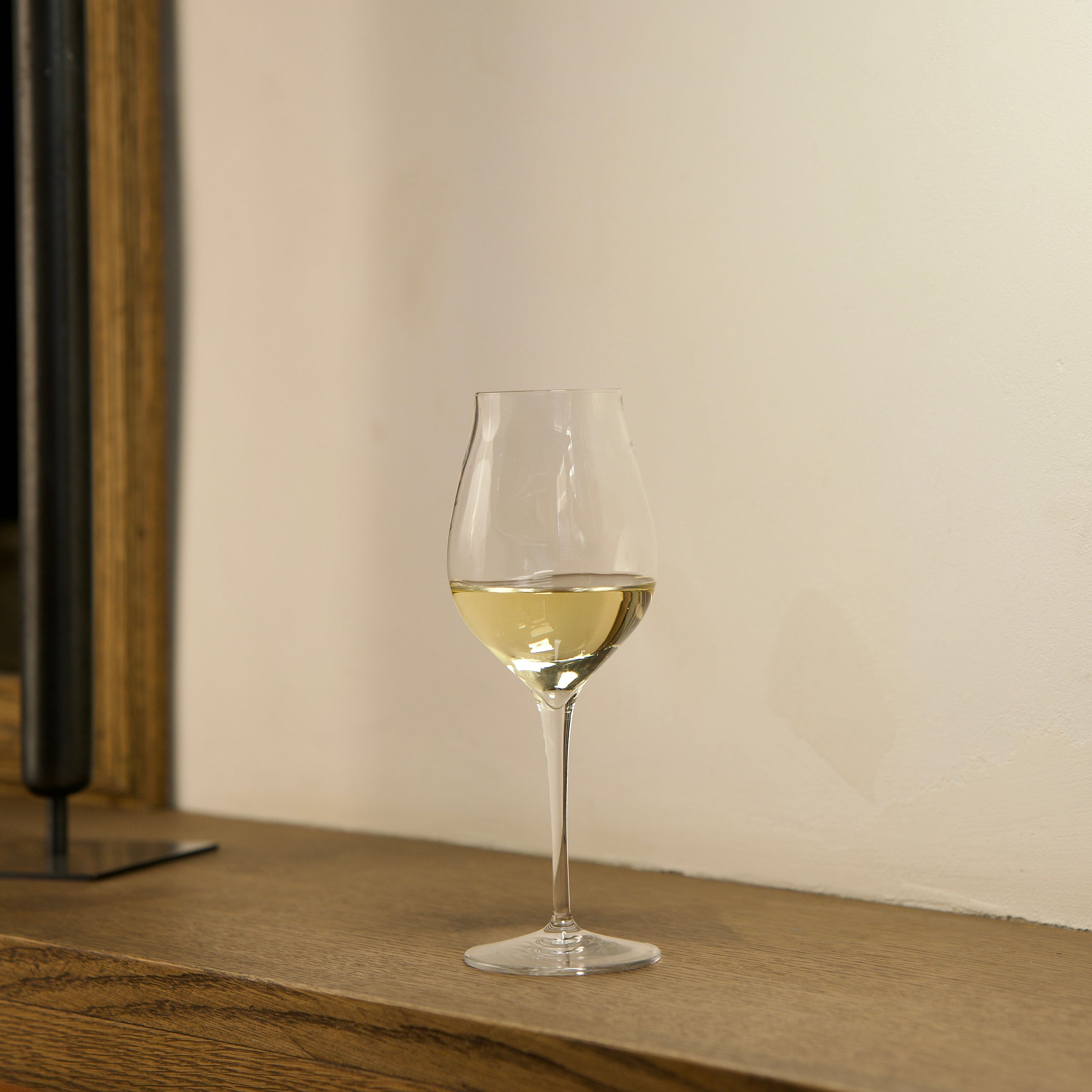 Vinea Malvasia wine glass filled with white wine on a wooden surface and a ivory background
