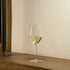 Vinea Malvasia wine glass filled with white wine on a wooden surface and a ivory background