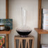Vinea wine decanter filled with red wine standing on a side table and various items on shelves around it