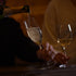 Hand holding Vinea Prosecco glass that is being filled with Sparkling wine on a dark background.