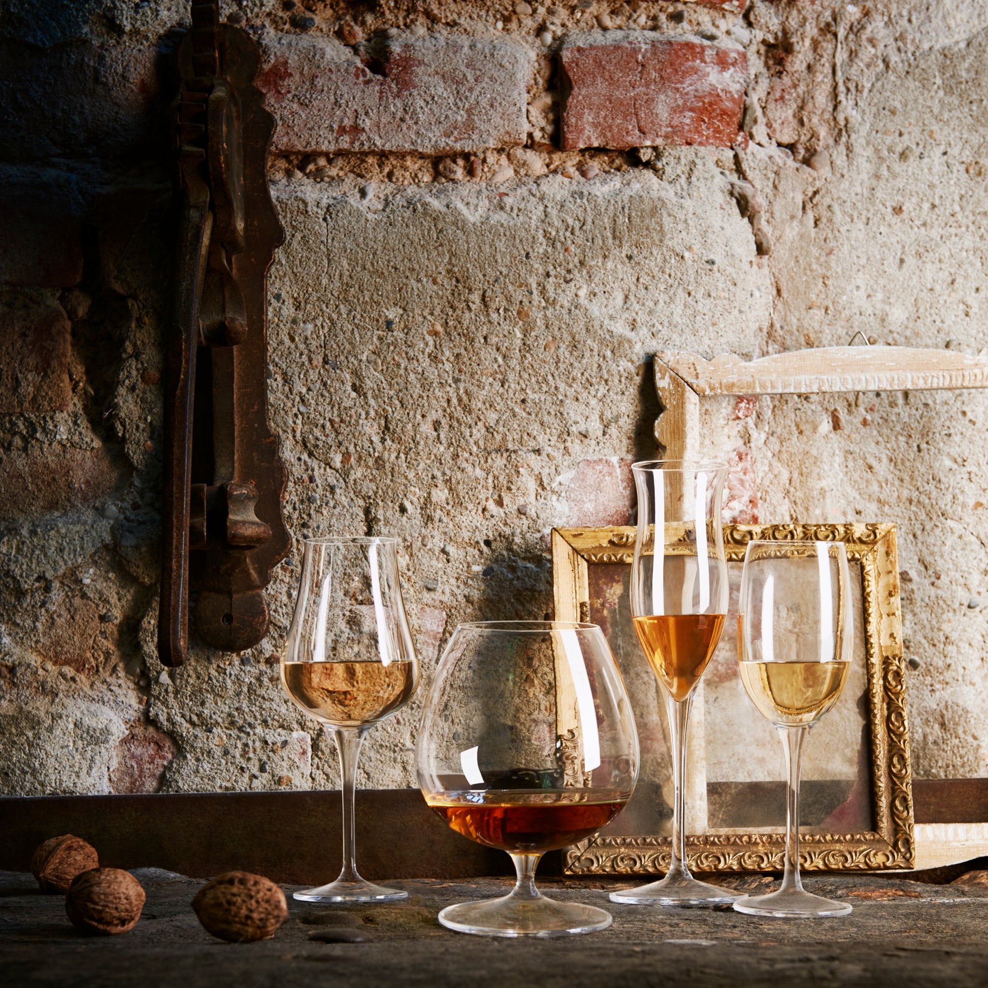 Vinoteque Cognac glass filled with a spirit standing next to other filled spirit glasses in the collection on a rustic wall background