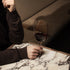 Hand holding Crescendo Bordeaux Red Wine Glass filled with red wine on a marble table and a dark background