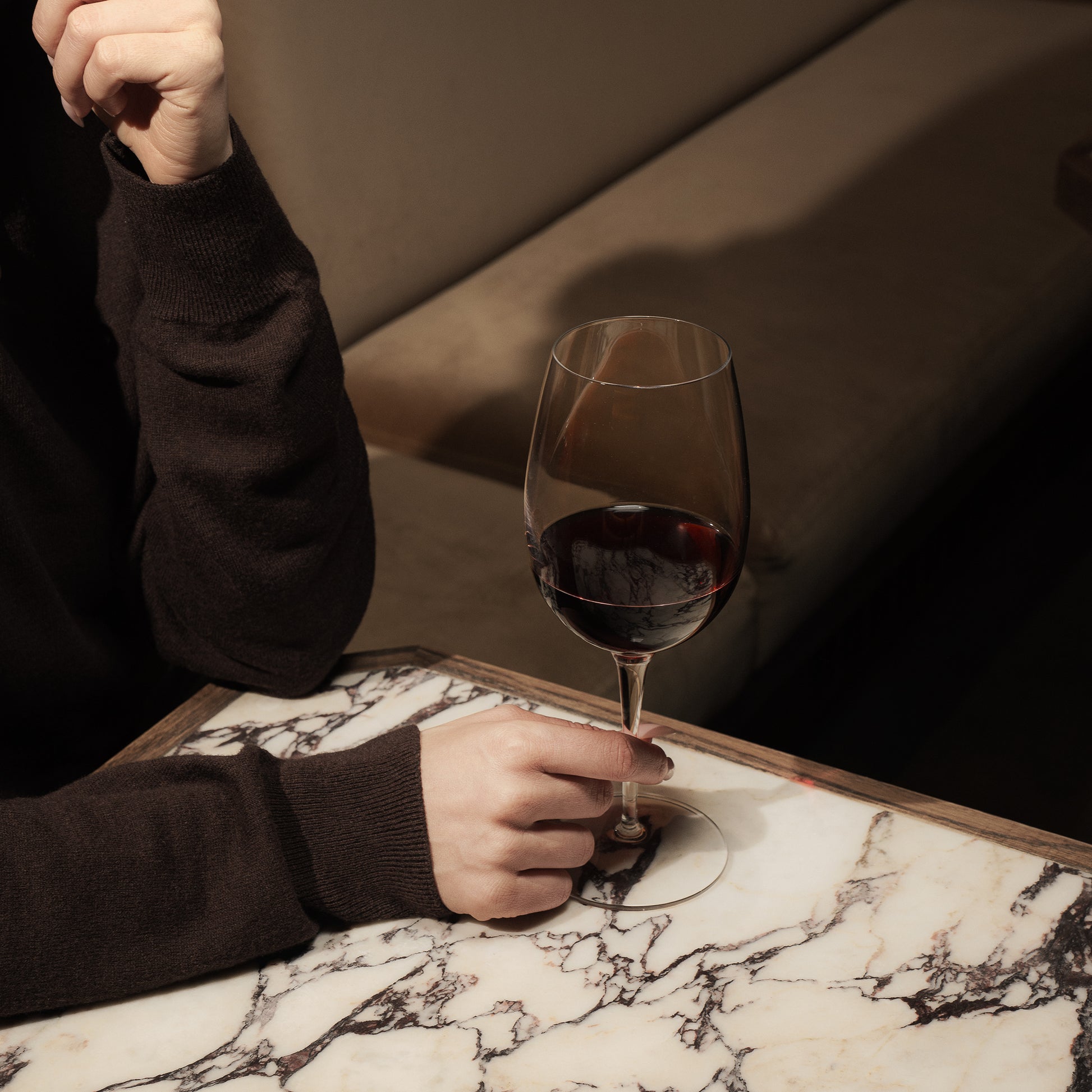 Hand holding Crescendo Bordeaux Red Wine Glass filled with red wine on a marble table and a dark background