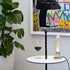 Vinoteque Riserva Red Wine Glass filled with red wine standing on a small white table next to a modern lamp, colorful graffiti painting and a plant in the background