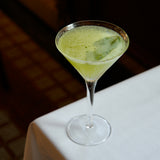 Green cocktail in a martini glass on a white surface with a dark background