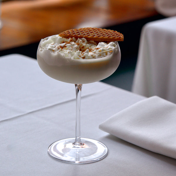 Milkshake with whipped cream and a cookie on top, served in a glass on a table.