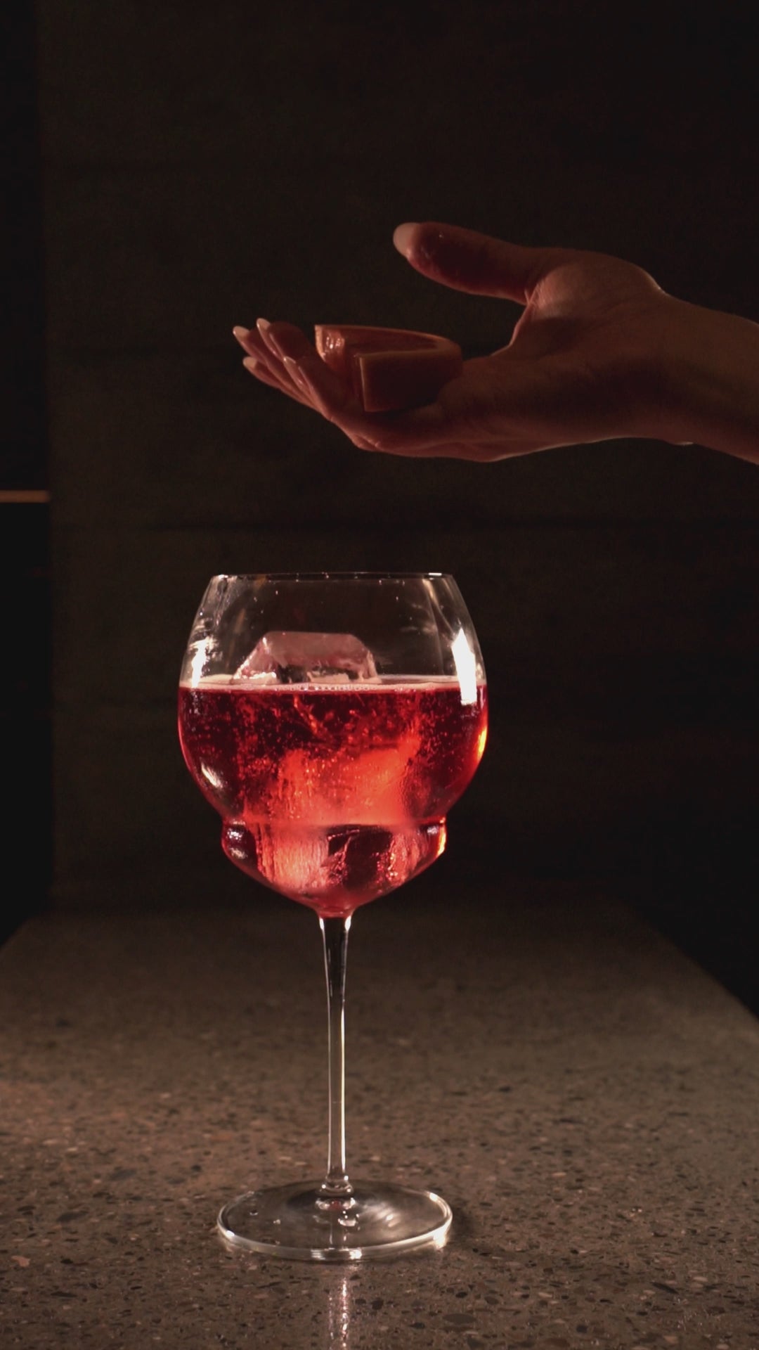 Video of a hand squeezing an orange slice into a Backdoor '20s Gin & Tonic glass filled with Aperol Spritz 