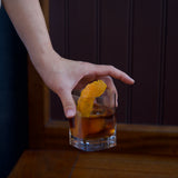 Hand holding a glass of cocktail with a lemon twist against a dark background
