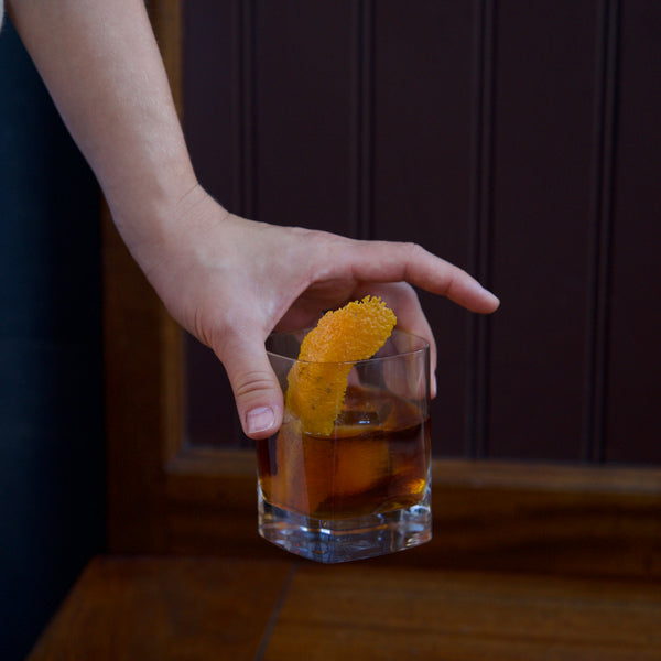 Hand holding a glass of cocktail with a lemon twist against a dark background