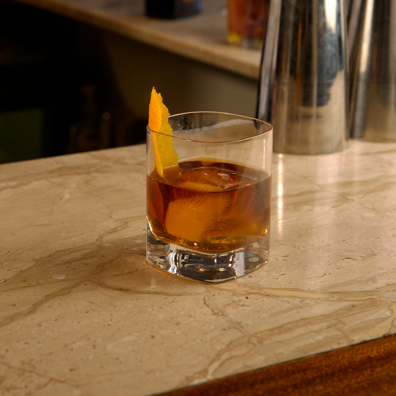 Glass of whiskey with an orange peel on a marble countertop