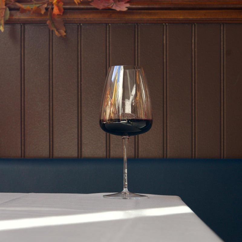 Wine glass with red wine on a white surface against a brown paneled wall