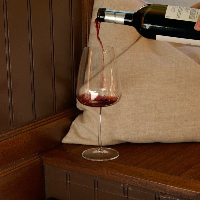 Red wine being poured into a glass on a wooden surface with a neutral background
