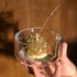 Hand holding a small glass bowl with a dessert resembling a mountain, with a blurred background.